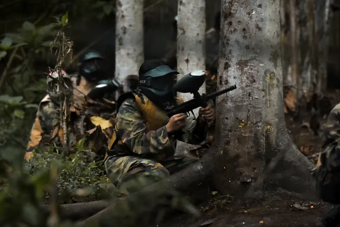 Peserta paintball berlindung di balik pohon sambil membidik