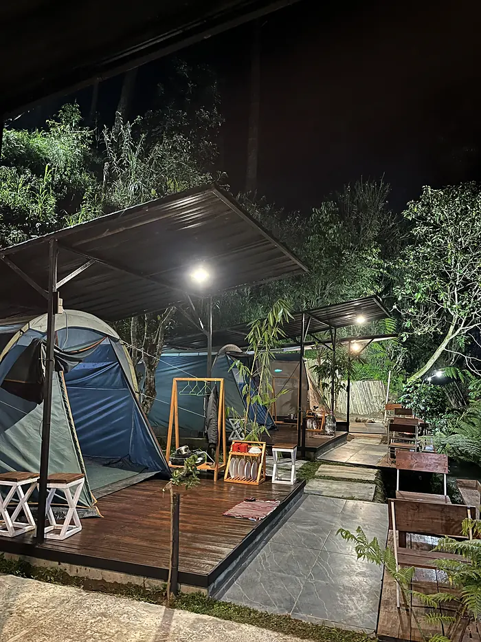 Tenda di atas deck kayu beratap yang disinari lampu pada malam hari